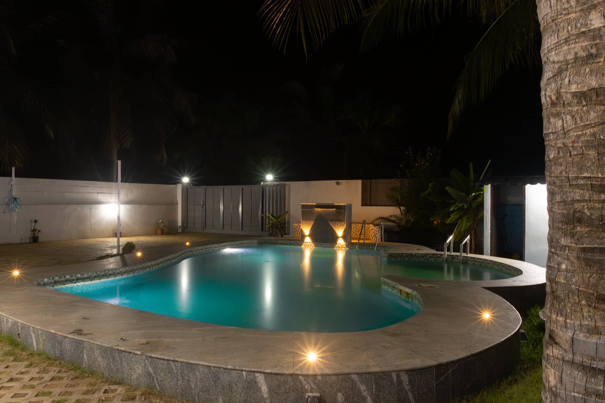 An illuminated outdoor swimming pool at night surrounded by warm deck lighting.