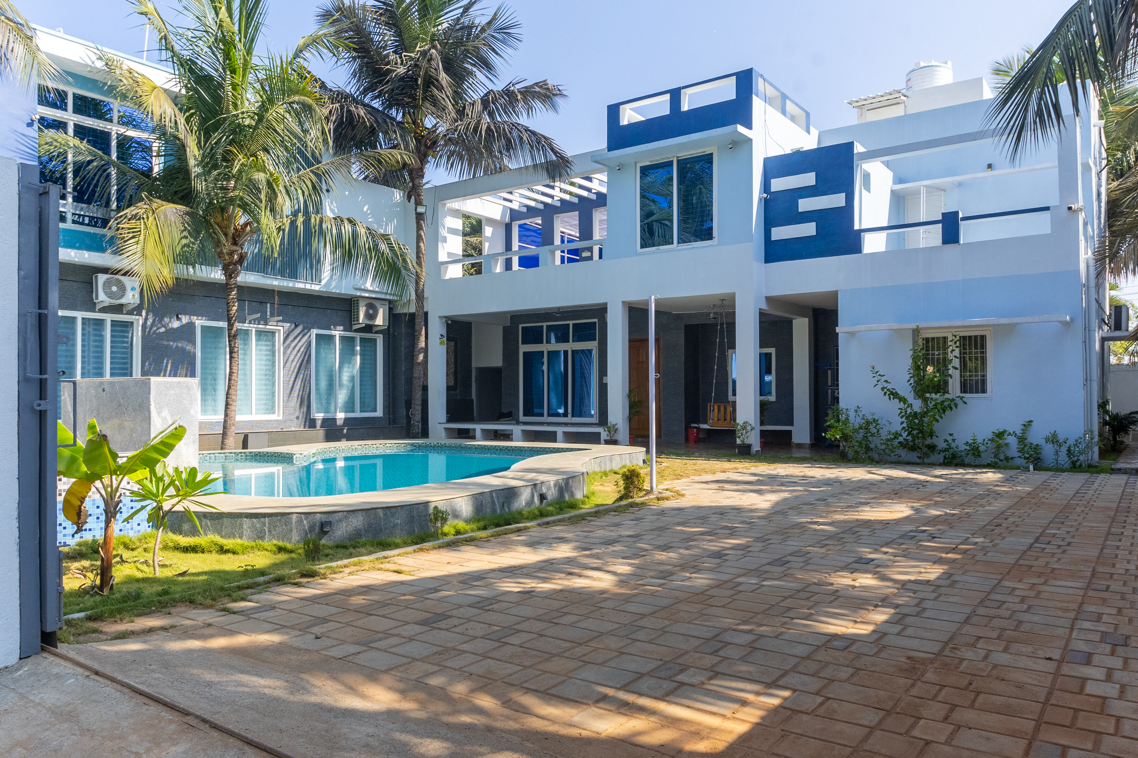 Modern blue and white two-story villa with a swimming pool and paved courtyard.