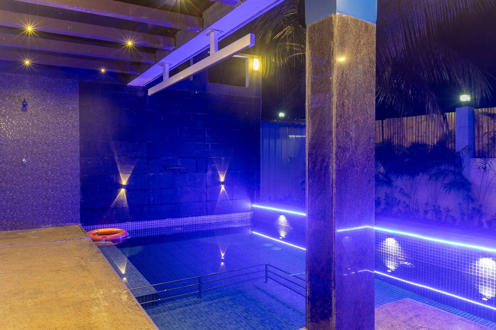 A swimming pool glowing with vibrant blue ambient lighting and wall sconces at night.