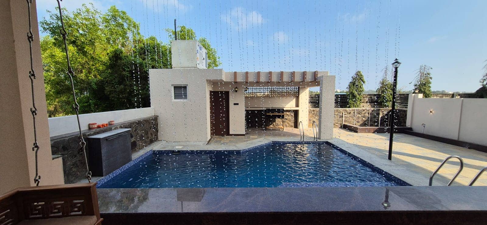 An outdoor swimming pool with a water curtain feature and poolside patio structure.