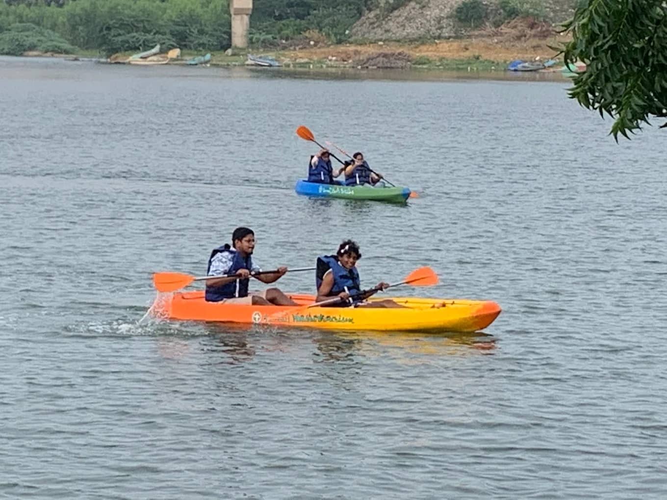People wearing life jackets paddling colorful kayaks on a calm river.